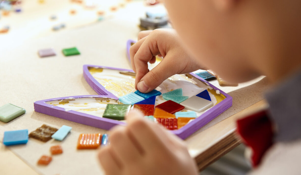 The mosaic puzzle art for kids, children's creative game. The hands are playing mosaic at table. Colorful multi-colored details close up. Creativity, children's development and learning concept